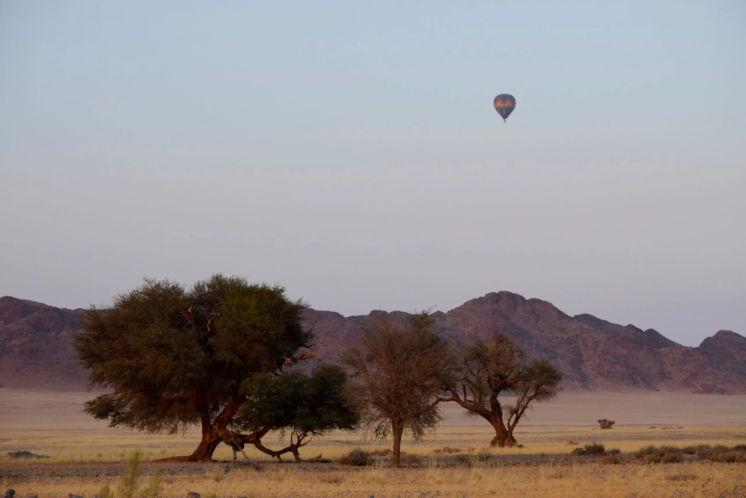 A lone balloon drifting over the savannah with a mountain range in the distance