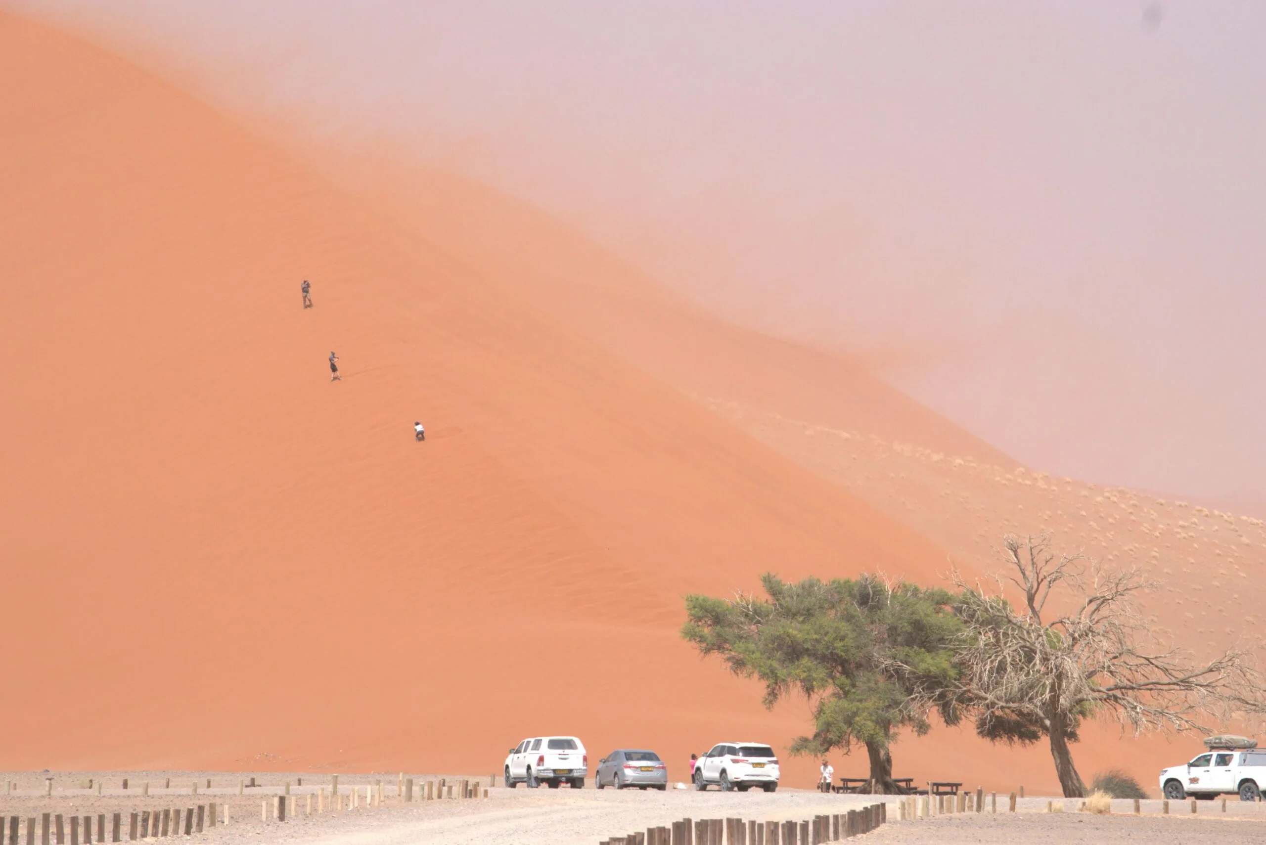Cars parked at the base of Dune 7 near Walvis Bay while three tourists make their way up the slope
