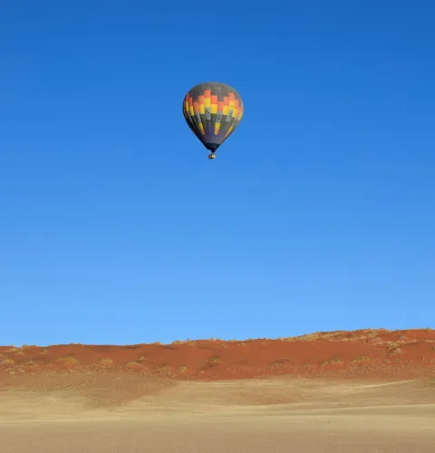 A hot air balloon floating above the Namib Desert dunes at sunrise