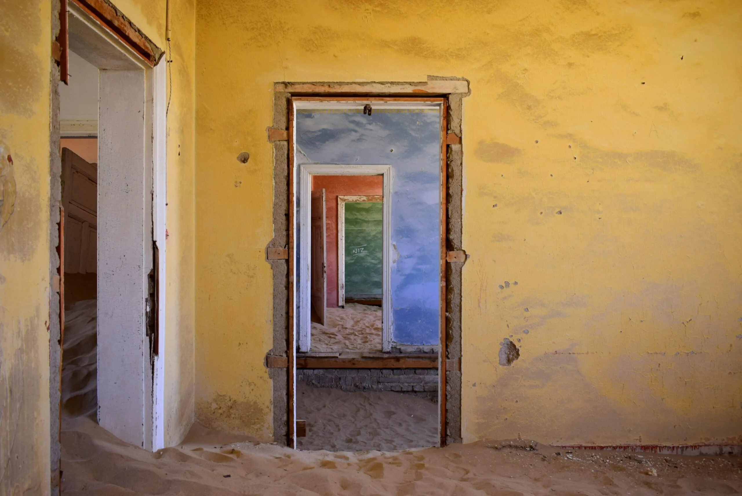 Sand-filled corridor of an abandoned Kolmanskop building, walls still showing faded original paint