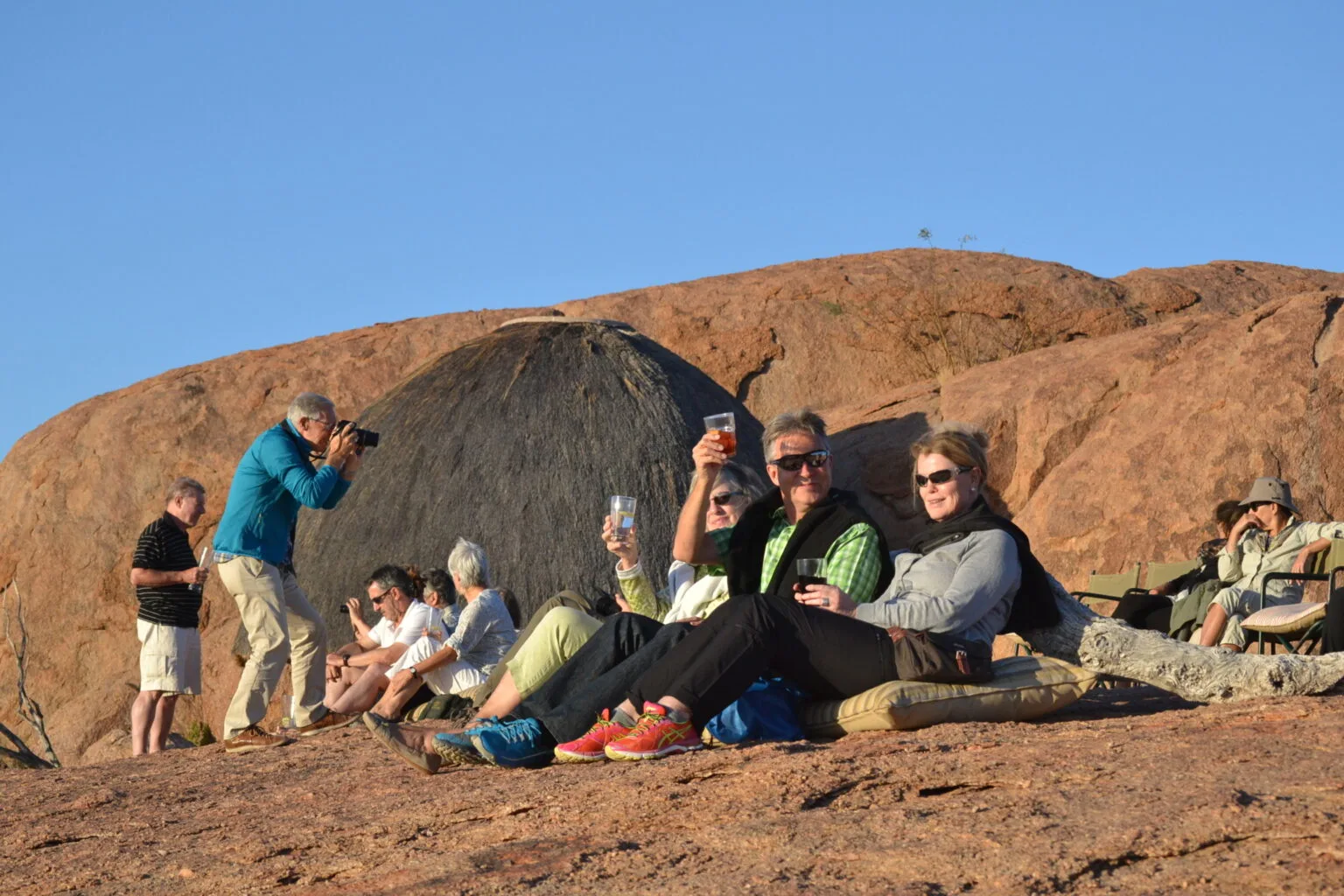 Tourists relaxing on a rock in the Namibian sunshine, one photographing the landscape with a DSLR camera